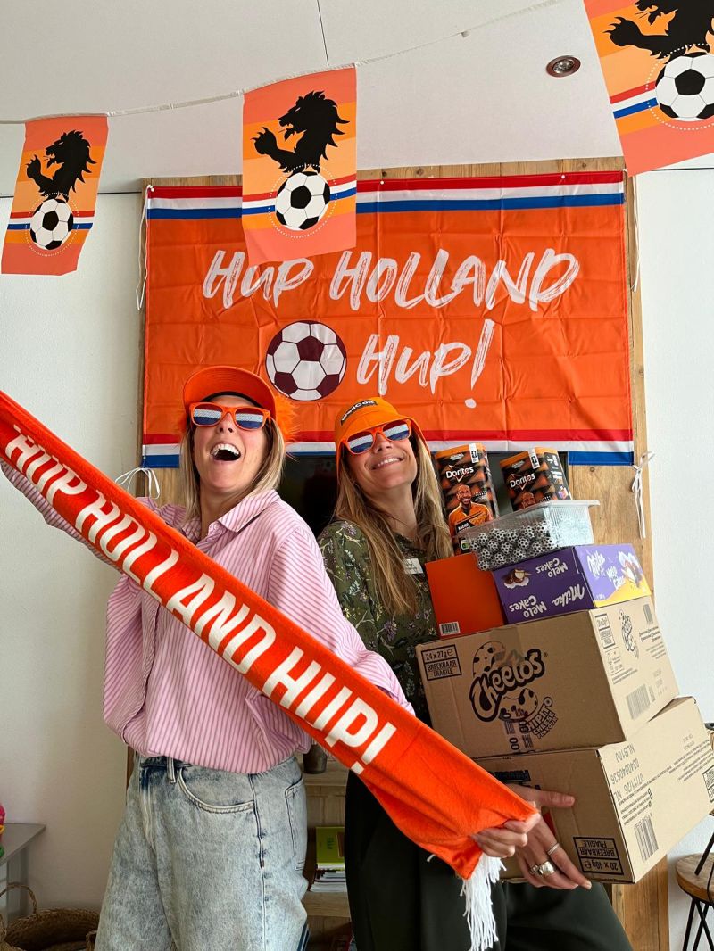 Medewerkers van WellColl vieren voetbal op kantoor met oranje versiering.