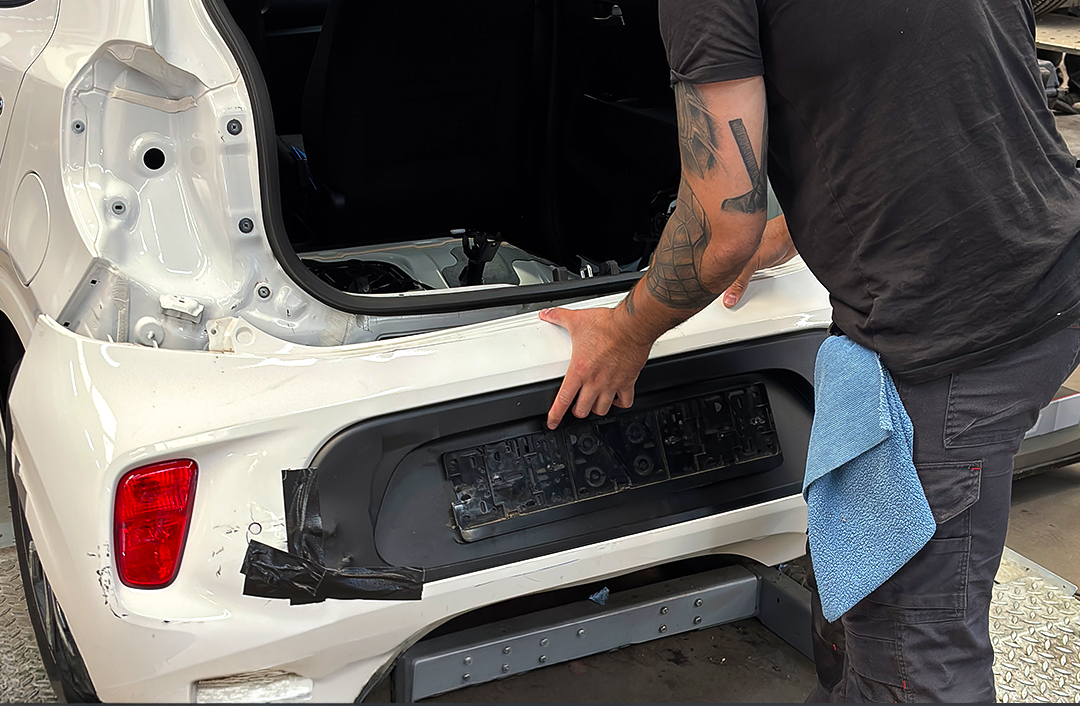 Monteur herstelt de achterbumper van een witte auto bij WellColl.